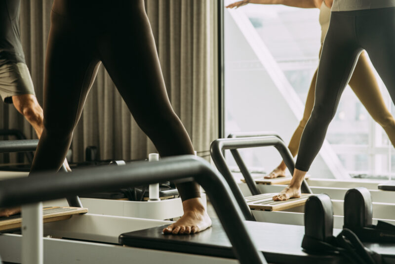 People standing wide feet a part on reformer bed