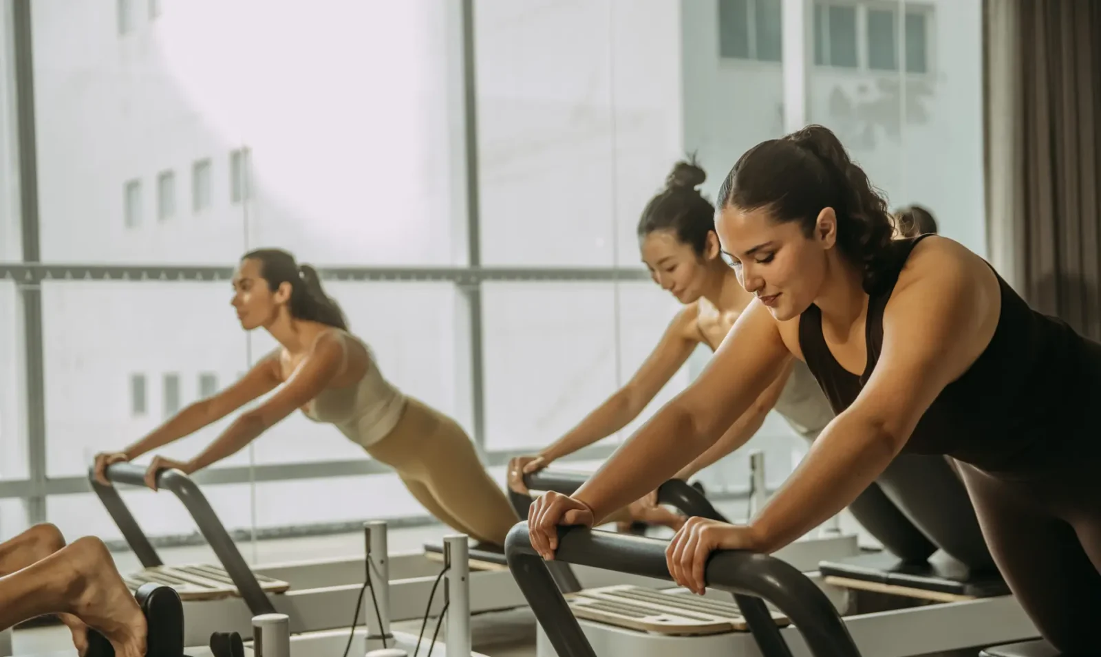 People on reformer bed holding position with arms on bar