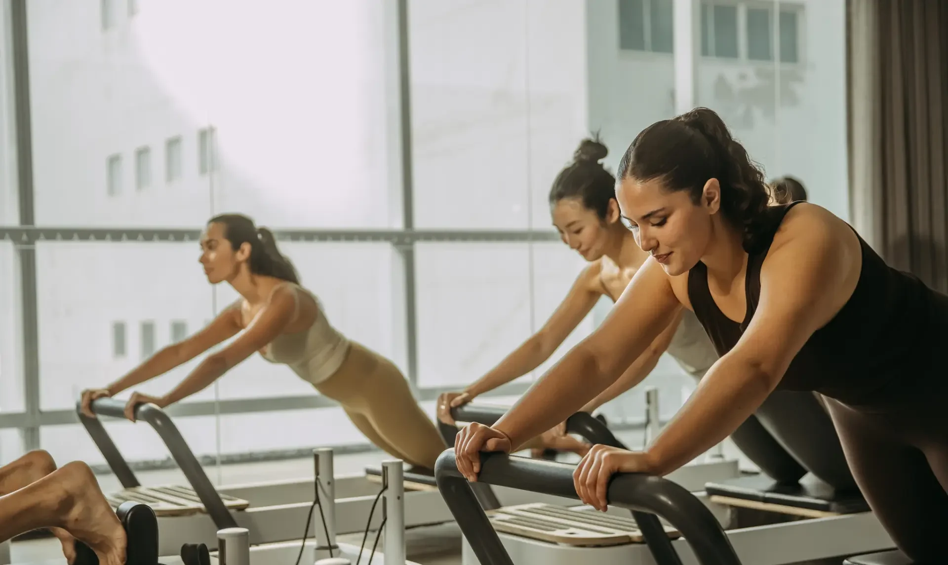 People on reformer bed holding position with arms on bar